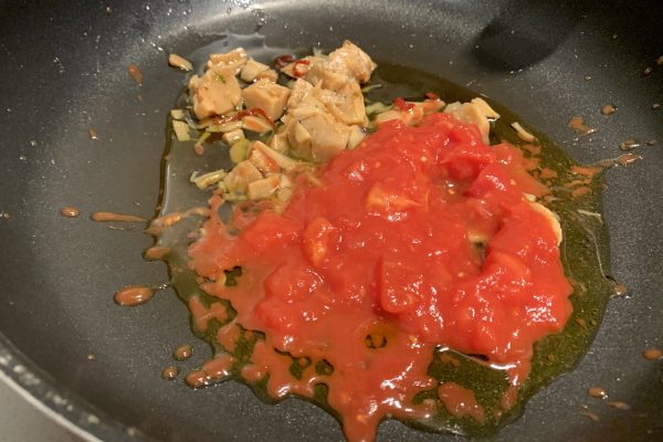 火にかけたフライパンに、女川アヒージョプリプリほたてとホールトマトを缶の半分入れる。 (この時、パスタは茹でておく)